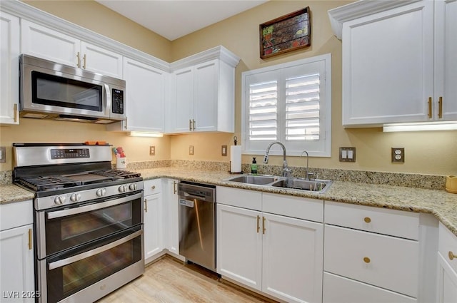 kitchen with light stone counters, a sink, white cabinetry, light wood-style floors, and appliances with stainless steel finishes