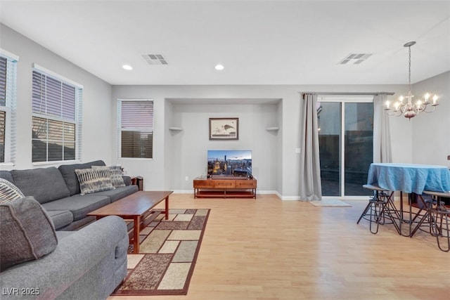 living room with light wood-style floors, baseboards, visible vents, and an inviting chandelier