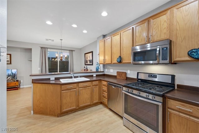 kitchen with dark countertops, appliances with stainless steel finishes, decorative light fixtures, a peninsula, and a sink