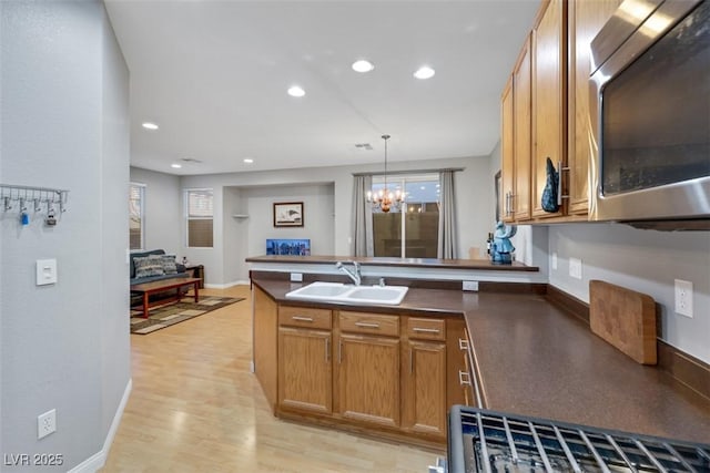 kitchen with a sink, brown cabinets, stainless steel microwave, dark countertops, and decorative light fixtures