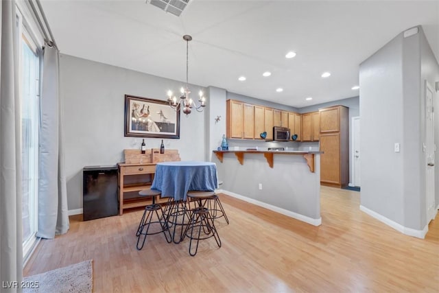 kitchen featuring a peninsula, a breakfast bar, visible vents, light wood-style floors, and stainless steel microwave