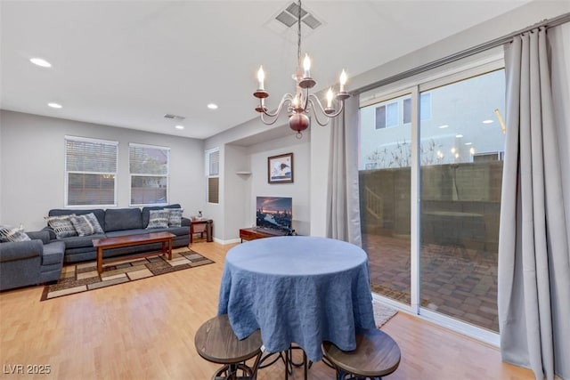 dining room with an inviting chandelier, a warm lit fireplace, visible vents, and wood finished floors