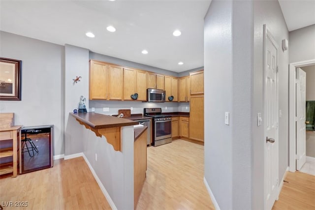 kitchen with dark countertops, a kitchen breakfast bar, a peninsula, stainless steel appliances, and light wood-style floors