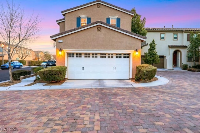 view of front of house featuring decorative driveway, a tile roof, an attached garage, and stucco siding