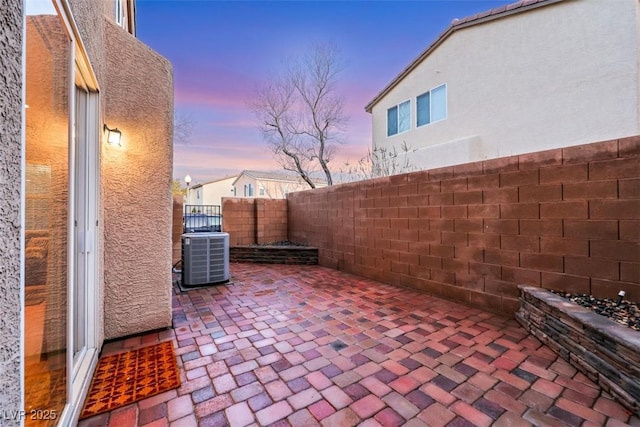 patio terrace at dusk featuring cooling unit and a fenced backyard