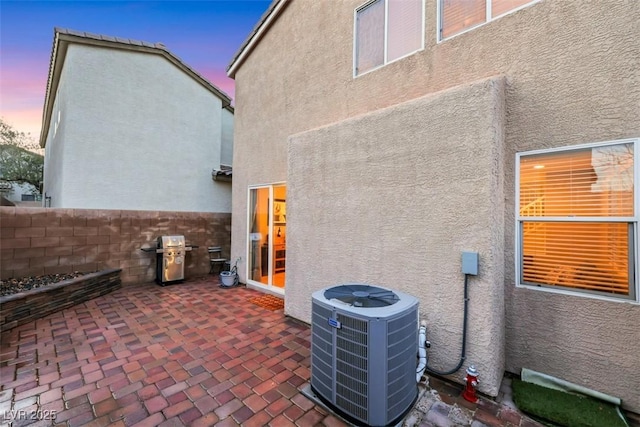 property exterior at dusk with a patio, fence, cooling unit, and stucco siding