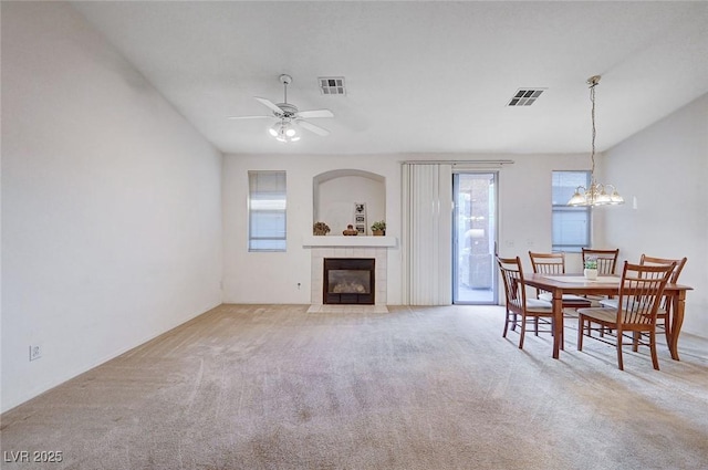 carpeted dining room with a fireplace, visible vents, and ceiling fan with notable chandelier