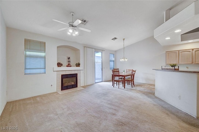 living room with lofted ceiling, light colored carpet, ceiling fan with notable chandelier, visible vents, and a tiled fireplace