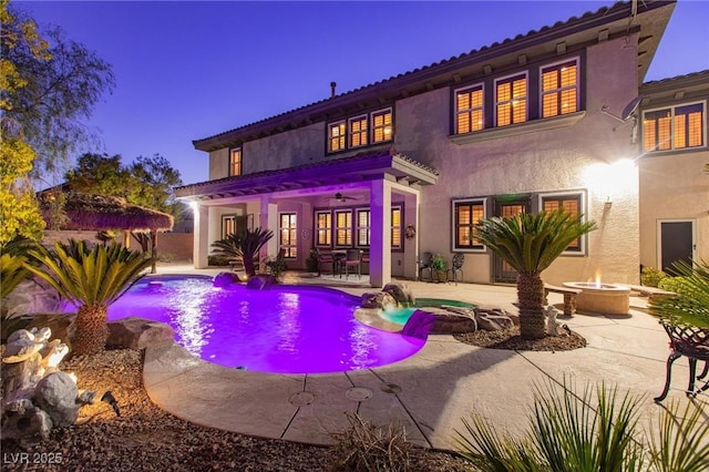 back of house featuring an outdoor pool, a patio, a fire pit, and stucco siding