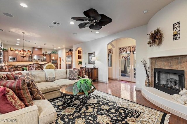 living room featuring arched walkways, visible vents, a tile fireplace, and wood finished floors