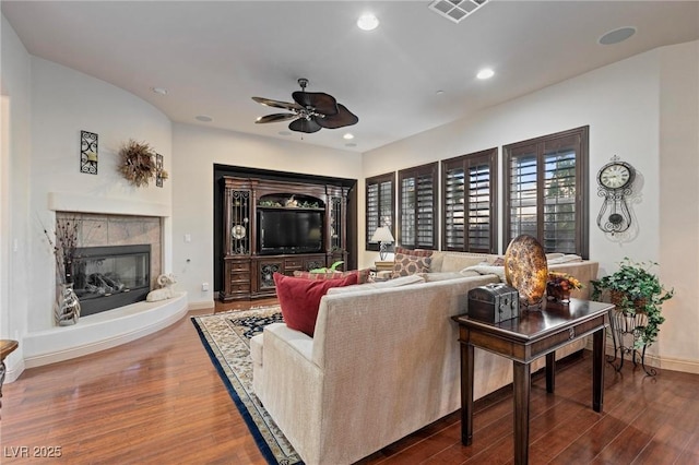 living area with visible vents, wood finished floors, a tile fireplace, and a ceiling fan