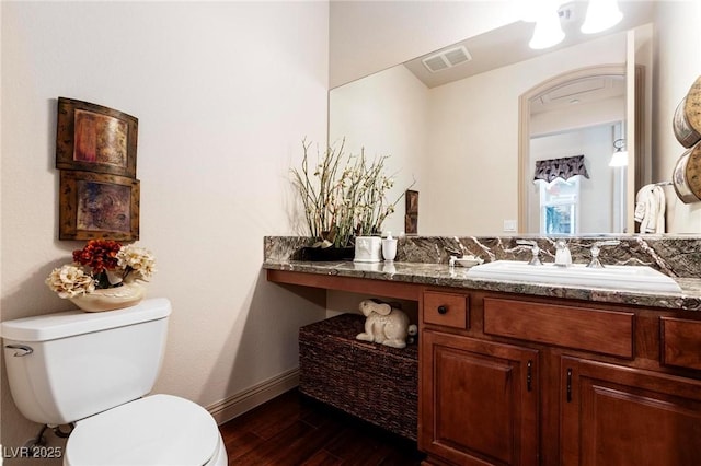 half bath with toilet, wood finished floors, vanity, visible vents, and baseboards