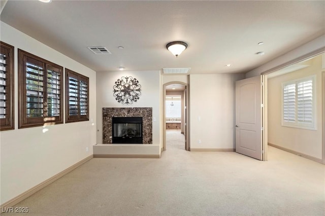 unfurnished living room featuring carpet, visible vents, baseboards, and a high end fireplace