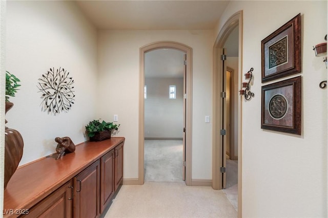 hallway featuring arched walkways, light colored carpet, and baseboards