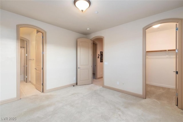 unfurnished bedroom featuring arched walkways, a spacious closet, light carpet, and baseboards