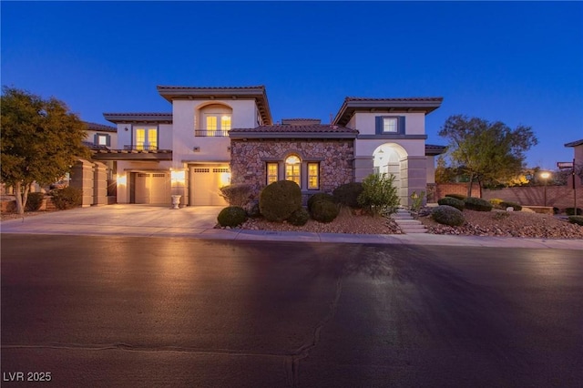 mediterranean / spanish-style home with a garage, stone siding, driveway, and stucco siding