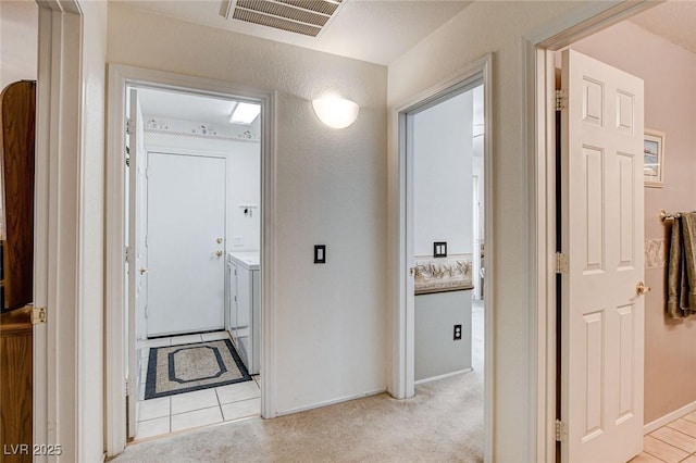 hallway with light tile patterned floors, light carpet, visible vents, and separate washer and dryer