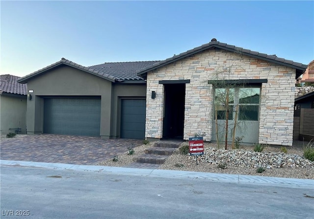 view of front facade featuring a garage, decorative driveway, a tiled roof, and stucco siding