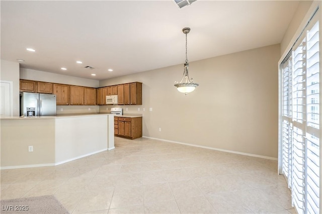 kitchen with white microwave, stainless steel fridge with ice dispenser, light countertops, hanging light fixtures, and brown cabinets