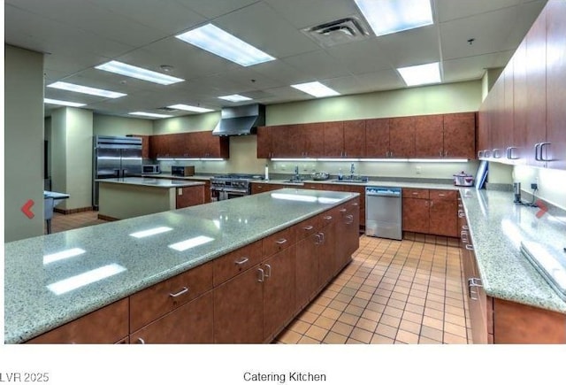 kitchen featuring a drop ceiling, stainless steel appliances, visible vents, a center island, and wall chimney exhaust hood