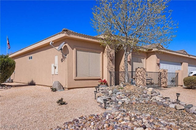 view of front of house with a garage, a tile roof, fence, and stucco siding