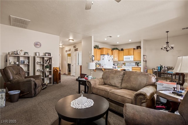 living room featuring a textured ceiling, visible vents, carpet flooring, and ceiling fan with notable chandelier