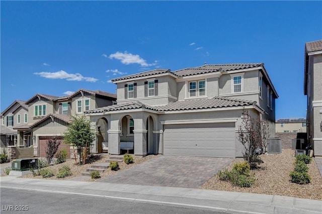 mediterranean / spanish home featuring decorative driveway, a tile roof, stucco siding, an attached garage, and central AC unit