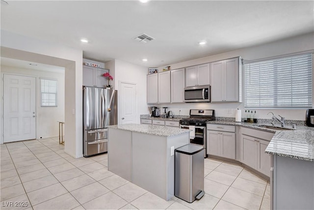 kitchen featuring light tile patterned floors, light stone counters, stainless steel appliances, a sink, and a kitchen island