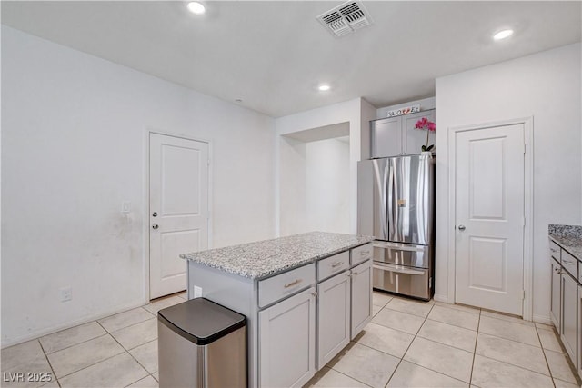 kitchen featuring a center island, visible vents, gray cabinets, freestanding refrigerator, and light stone countertops