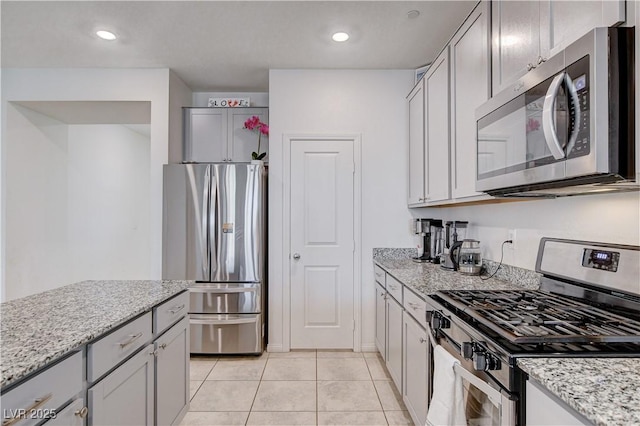 kitchen with stainless steel appliances, gray cabinetry, light stone counters, and light tile patterned floors