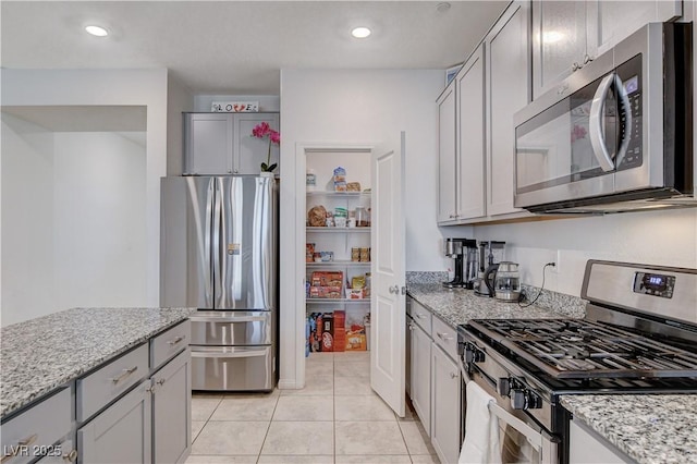 kitchen with gray cabinetry, stainless steel appliances, light tile patterned floors, and light stone countertops