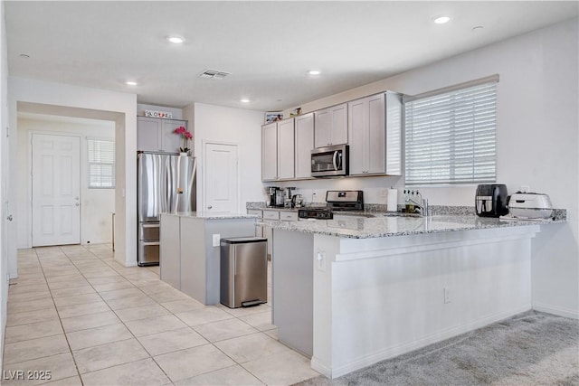 kitchen featuring light stone counters, a center island, visible vents, appliances with stainless steel finishes, and a peninsula