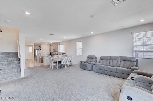 living area featuring light carpet, stairway, visible vents, and a healthy amount of sunlight