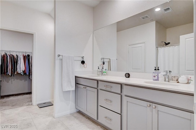 bathroom with a sink, visible vents, baseboards, double vanity, and a walk in closet