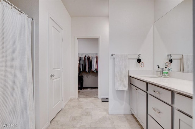 bathroom featuring tile patterned floors, baseboards, a walk in closet, and vanity