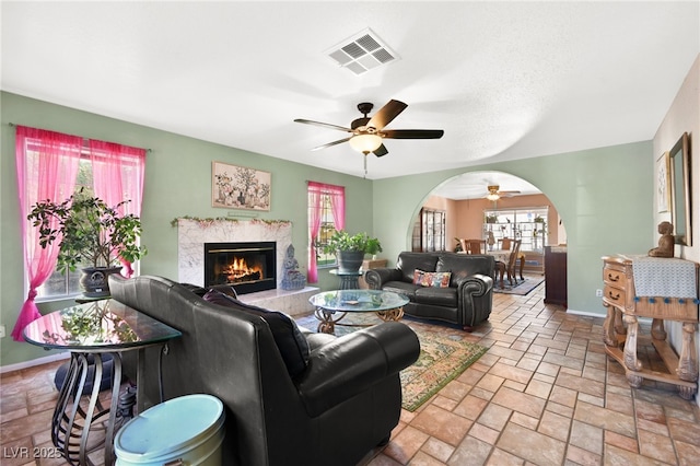 living area with arched walkways, stone tile flooring, visible vents, and baseboards