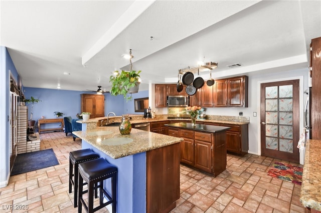 kitchen featuring visible vents, a breakfast bar area, a center island, stainless steel appliances, and stone tile flooring