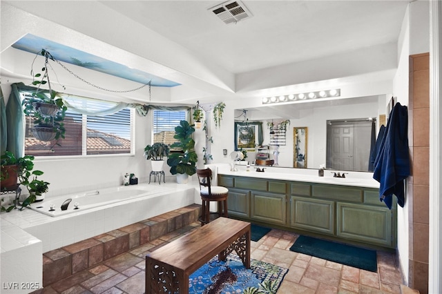 bathroom featuring double vanity, stone tile floors, visible vents, a garden tub, and a tray ceiling