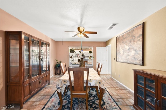 dining room featuring stone tile flooring, visible vents, ceiling fan, and baseboards