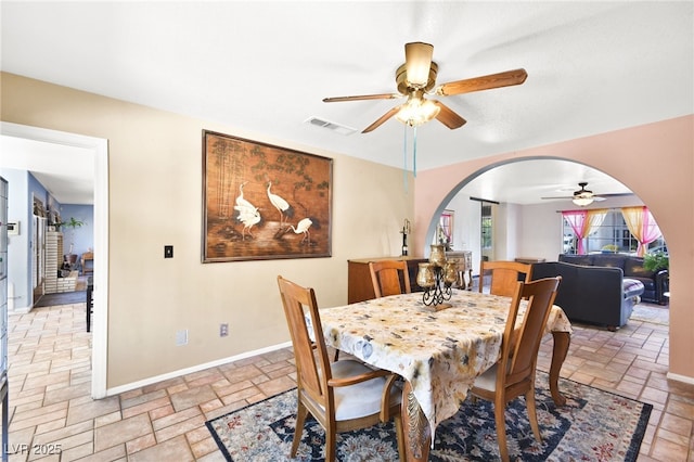 dining area with arched walkways, baseboards, visible vents, and stone tile floors