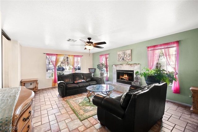 living area featuring a healthy amount of sunlight, a premium fireplace, visible vents, and stone tile floors