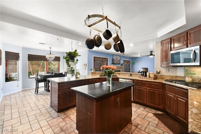 kitchen with stone tile floors, a kitchen island, a peninsula, hanging light fixtures, and stainless steel appliances