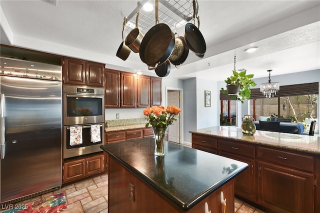 kitchen featuring decorative light fixtures, appliances with stainless steel finishes, a center island, stone tile flooring, and an inviting chandelier