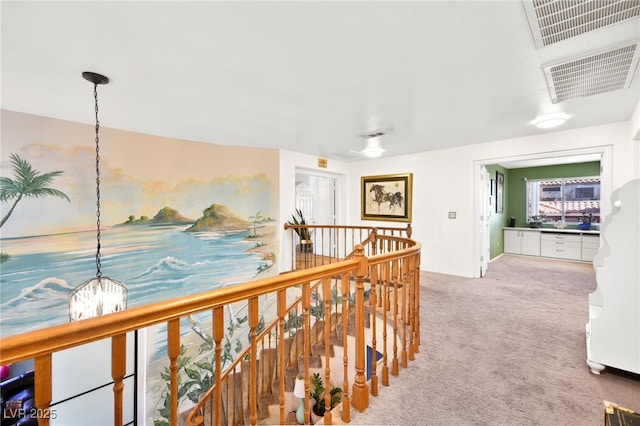 hall with carpet, visible vents, a notable chandelier, and an upstairs landing