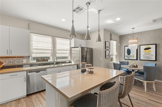 kitchen featuring stainless steel appliances, decorative light fixtures, visible vents, and white cabinets