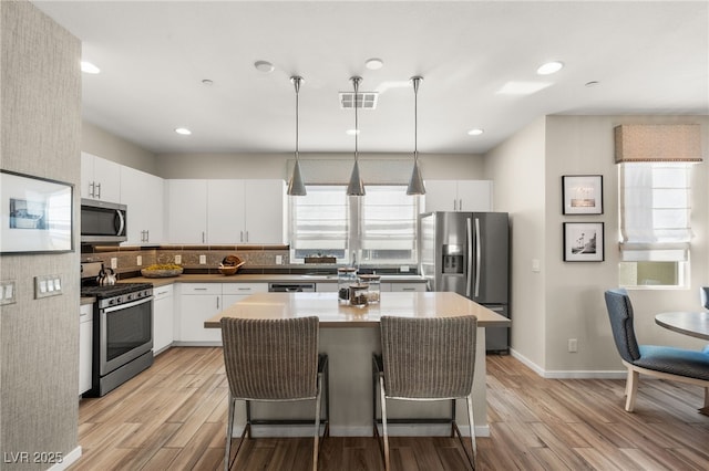 kitchen with stainless steel appliances, visible vents, white cabinetry, light wood-type flooring, and pendant lighting