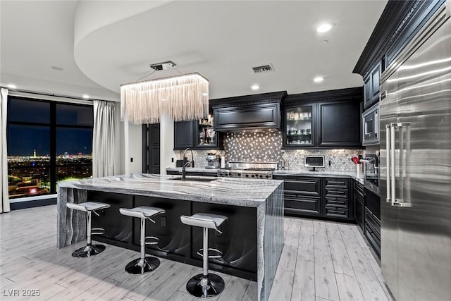 kitchen featuring visible vents, built in appliances, light stone countertops, premium range hood, and a sink