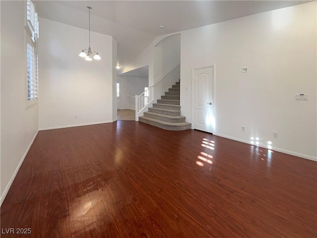 unfurnished living room with high vaulted ceiling, a notable chandelier, wood finished floors, baseboards, and stairway