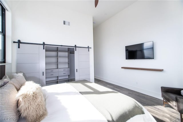 bedroom with a barn door, a ceiling fan, visible vents, baseboards, and dark wood finished floors