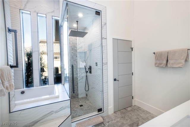 bathroom featuring a garden tub, a marble finish shower, and baseboards